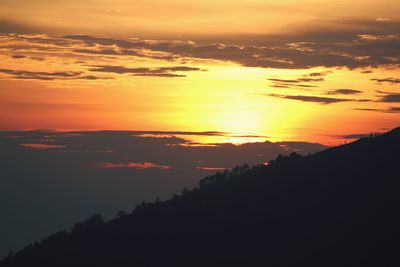 Scenic view of dramatic sky over silhouette landscape during sunset