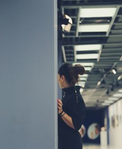 Side view of woman standing by wall in passage