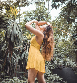 Profile view of young female model with hand in hair standing against trees
