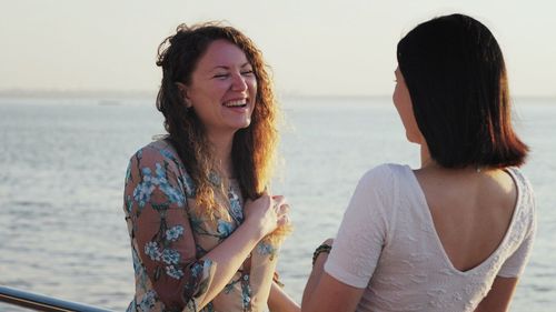 Cheerful woman talking to female friend while standing on boat by sea