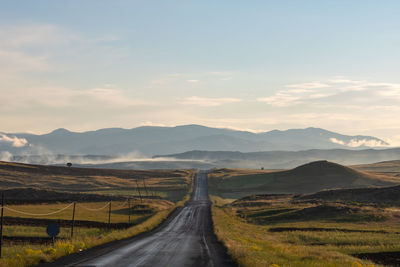 Country road leading towards mountains against sky