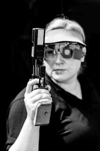 Woman holding gun against black background