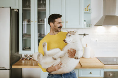 Man holding siberian husky in kitchen at home