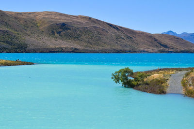 Scenic view of lake by mountains against clear blue sky