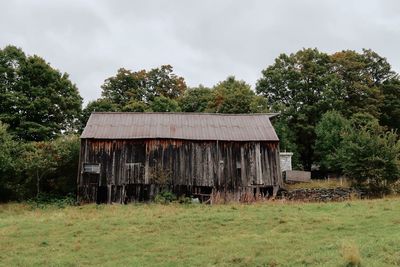 Old house on field by trees against sky