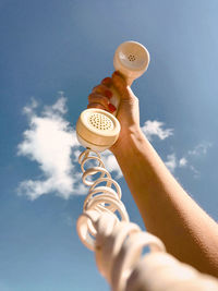 Low angle view of hand holding drink against blue sky