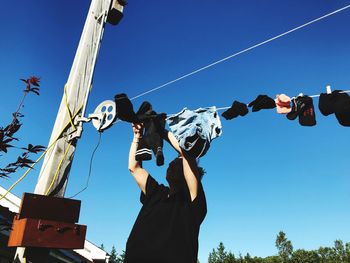 Low angle view of woman hanging clothes on clotheslines against clear blue sky