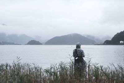 Rear view of man standing against lake during foggy weather