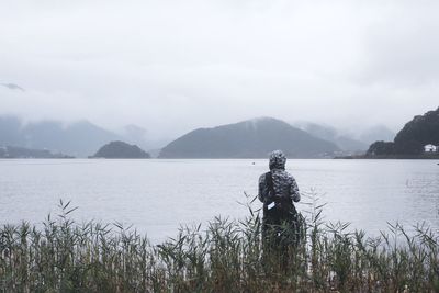 Rear view of man looking at lake against sky