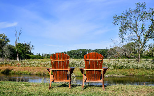 Empty chairs by lake against sky