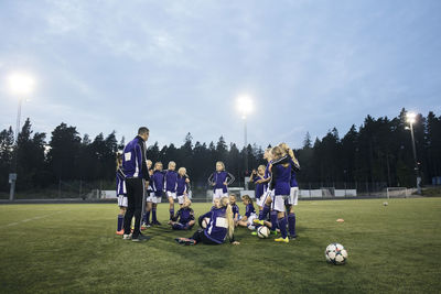 Coach standing by female soccer team on field against sky