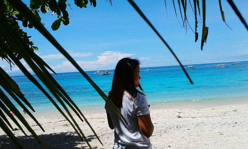 Rear view of woman standing on shore at beach against sky