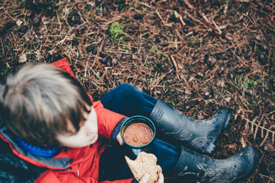 High angle view of boy eating food while sitting on field
