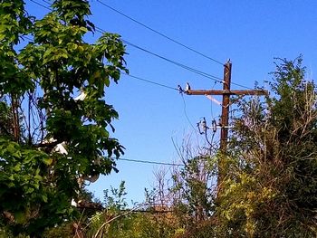 Low angle view of electricity pylon against clear blue sky