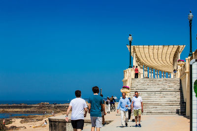 Rear view of people on beach against clear blue sky