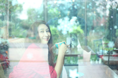 Portrait of smiling woman sitting in cafe seen through window