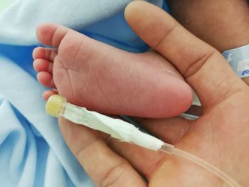 Close-up of hand with tube by baby foot on bed