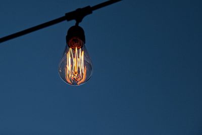 Low angle view of illuminated light bulb against clear blue sky