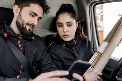 Young delivery man and woman using mobile phone in truck