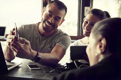 Smiling man using smart phone while women looking in cafe