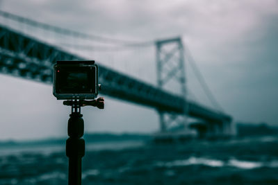 Close-up of tripod camera with onaruto bridge over sea in background