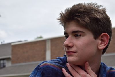 Close-up of young man looking away against sky