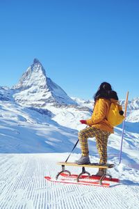 Side view of teenage girl tobogganing on snowcapped mountain against clear sky