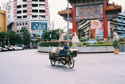 Full length of man riding bicycle cart on street against buildings in city