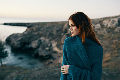 Young woman on rock at beach against sky