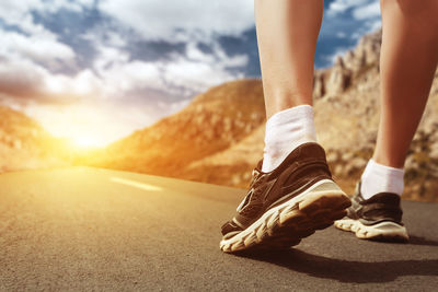 Low section of woman walking on road against sky