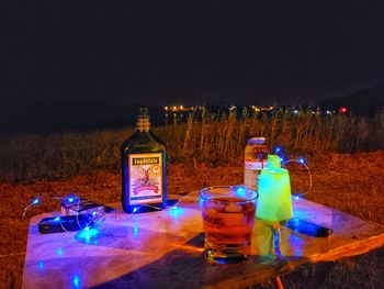 Illuminated bottles on table against sky at night