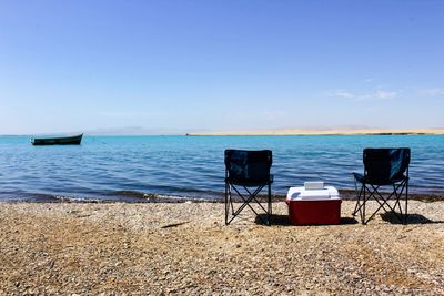 Chairs on beach against clear blue sky