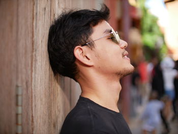 Close-up of young man wearing sunglasses against wooden wall