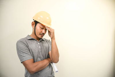 Depressed engineer with head in hand standing against wall