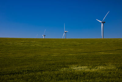 Windmill on field against clear blue sky