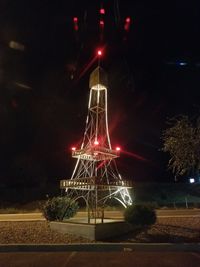 Illuminated lights by trees against sky at night