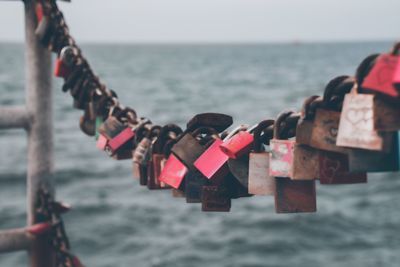 Love locks hanging on chain against sea and sky