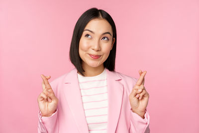 Portrait of young woman gesturing against pink background