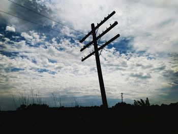 Low angle view of electricity pylon against cloudy sky