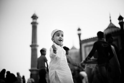 Low angle view of cute boy wearing traditional clothing standing outdoors against mosque