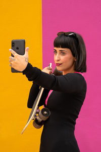 Beautiful woman with short hair posing with a skateboard on a colored background