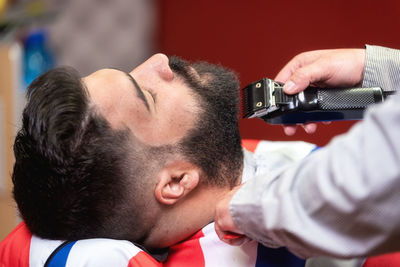 Cropped hands of barber shaving male customer beard in salon