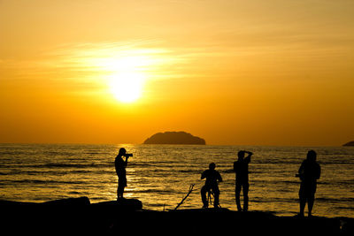 Silhouette people on beach against sky during sunset