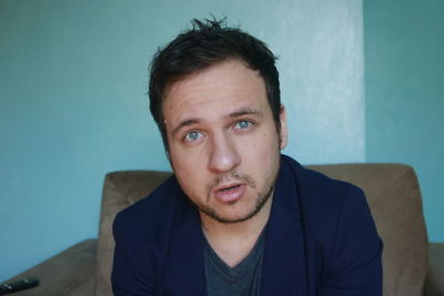 Portrait of young man sitting against wall