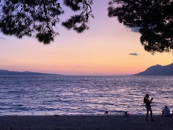 Silhouette people standing on beach against sky during sunset