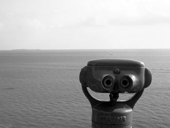 Close-up of coin-operated binoculars on sea against sky