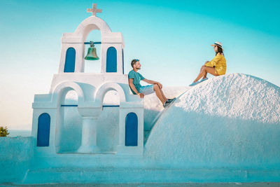 Couple talking while sitting by chapel against clear sky