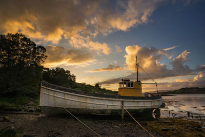 Boat moored on beach against sky during sunset