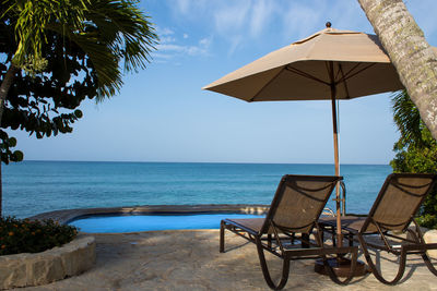 Chairs and table by swimming pool in sea against sky