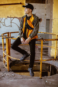 Young man looking away while sitting on wall